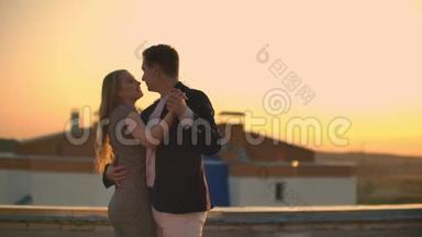 两个情人在日出日落时在俯瞰城市的摩天大楼上拥抱跳舞。 浪漫的场景。